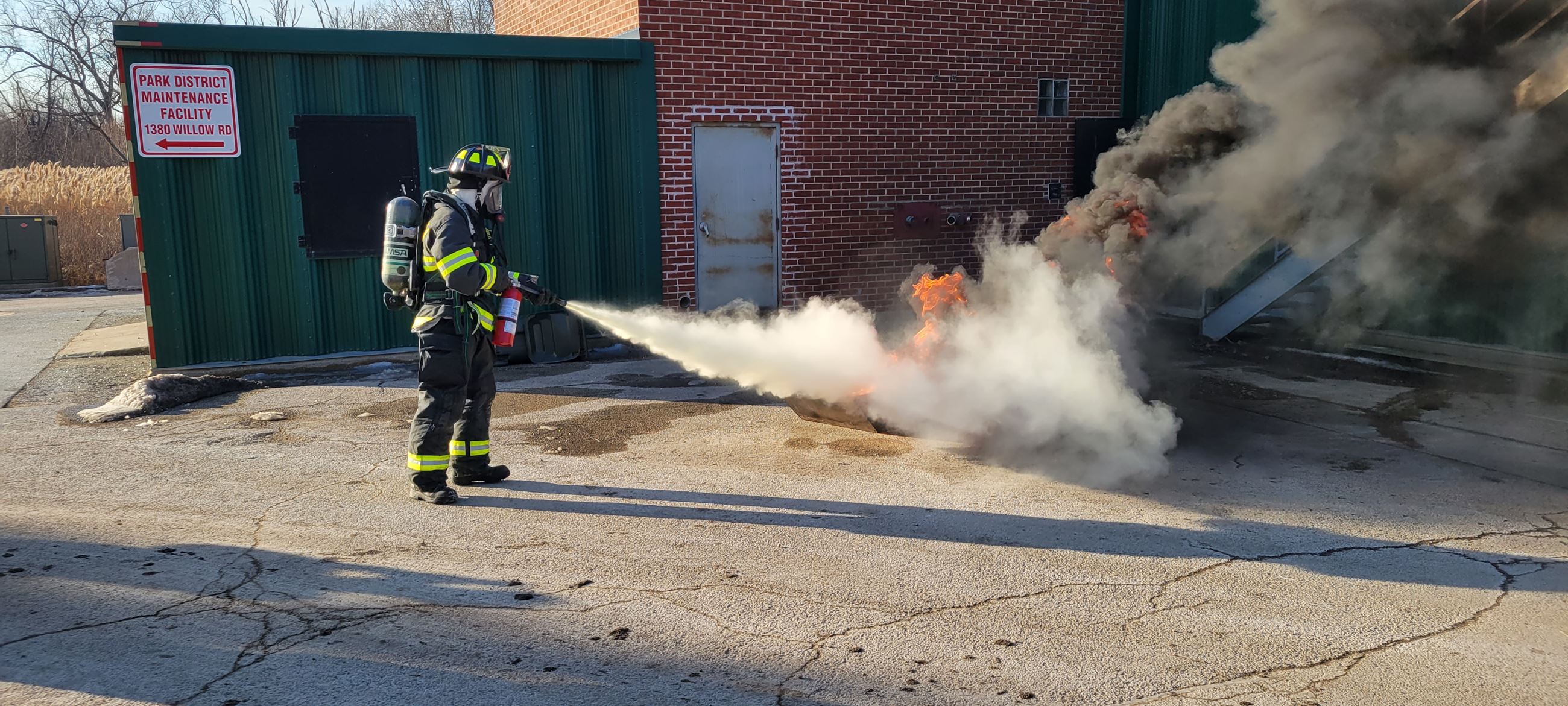 Firefighter discharging extinguisher on flame during training exercise.